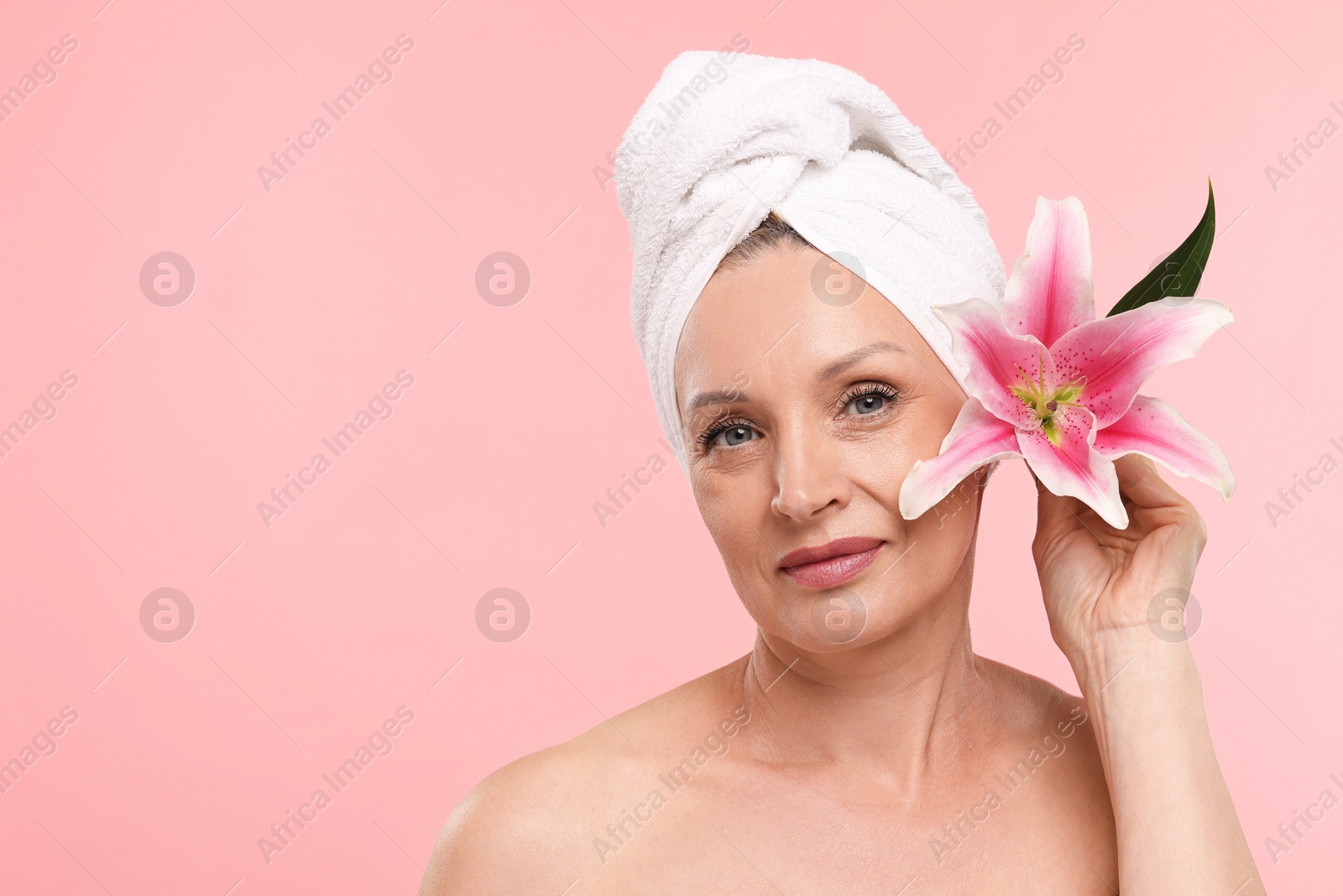 Beautiful woman with flower and towel wrapped on her head against light pink background. Space for text Photo of Beautiful woman with flower and towel wrapped on her head against light pink background. Space for text