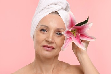 Photo of Beautiful woman with flower and towel wrapped on her head against light pink background