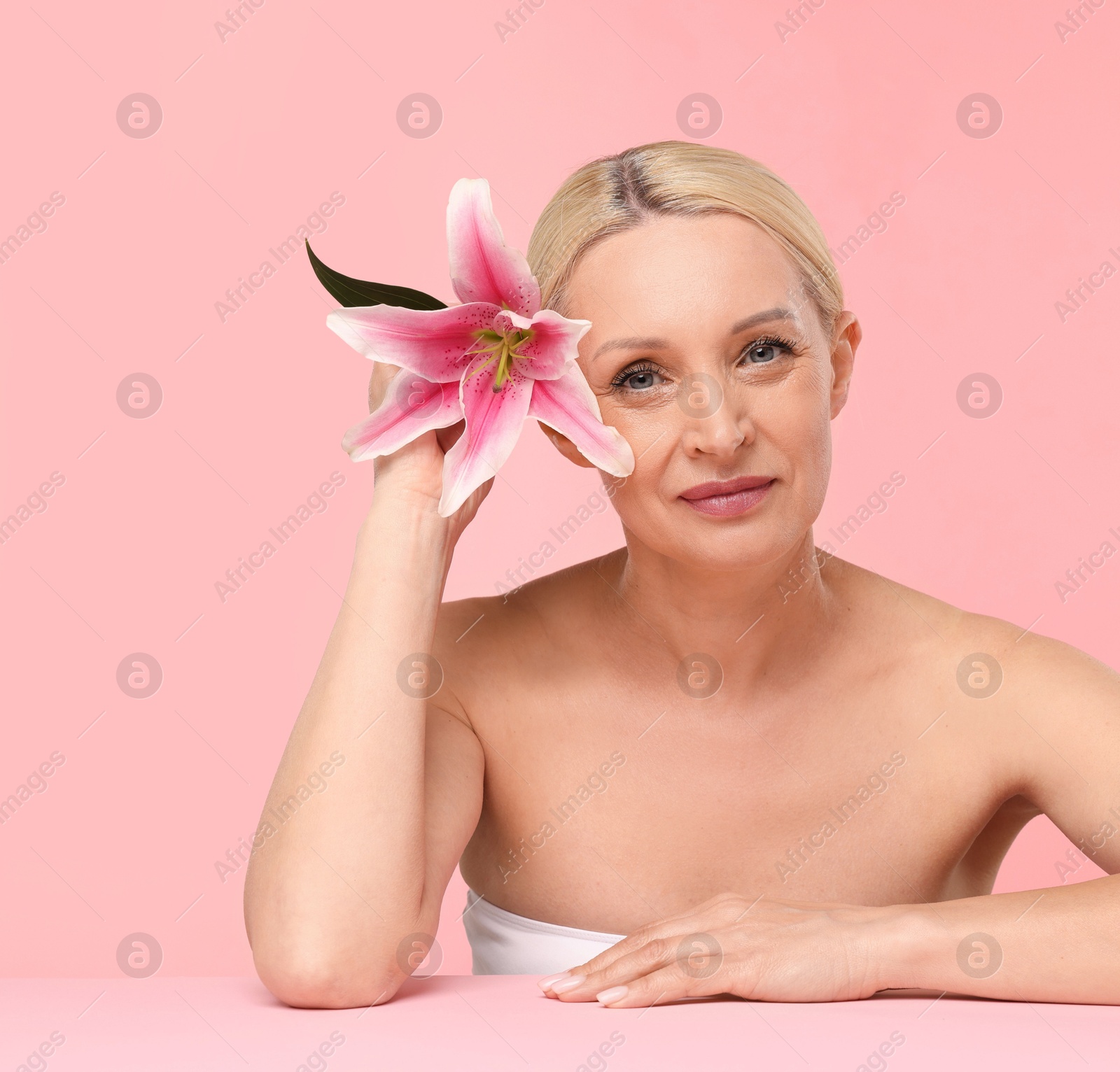 Beautiful woman with lily flower on light pink background Photo of Beautiful woman with lily flower on light pink background
