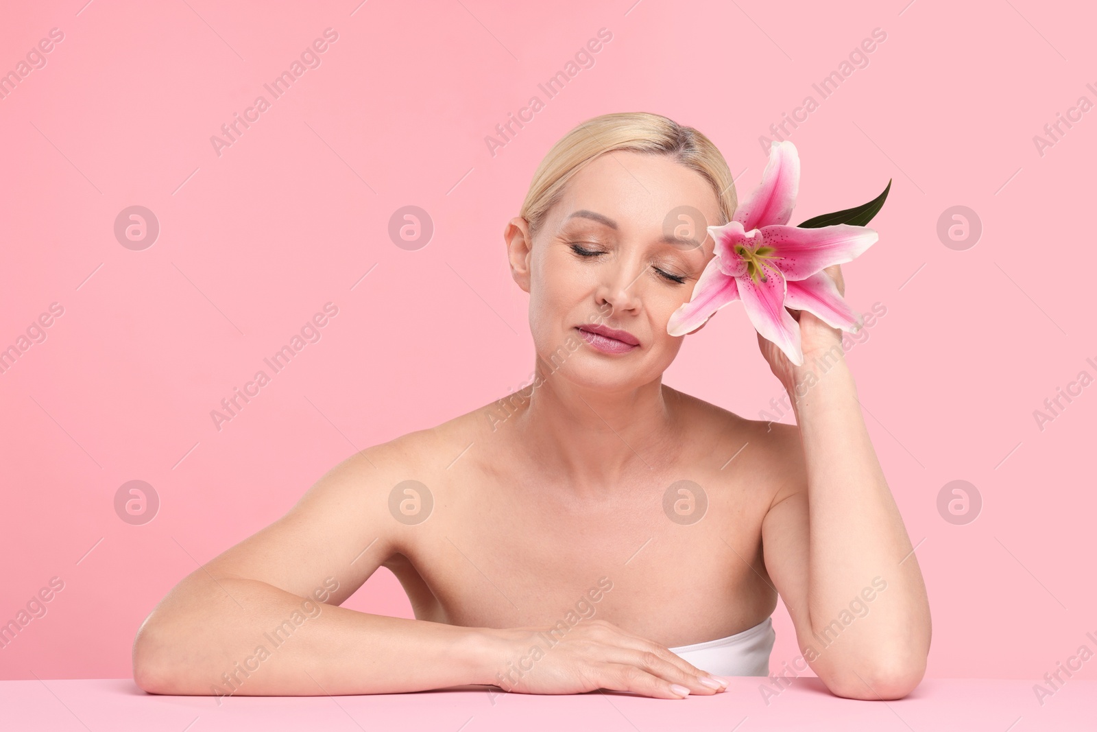 Beautiful woman with lily flower on light pink background Photo of Beautiful woman with lily flower on light pink background