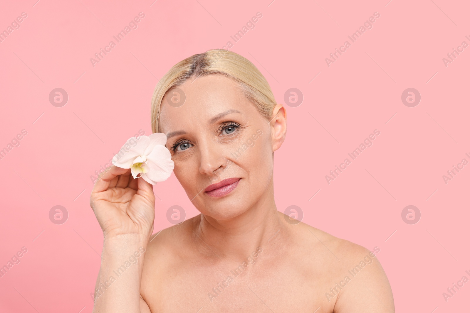 Beautiful woman with orchid flower on light pink background Photo of Beautiful woman with orchid flower on light pink background