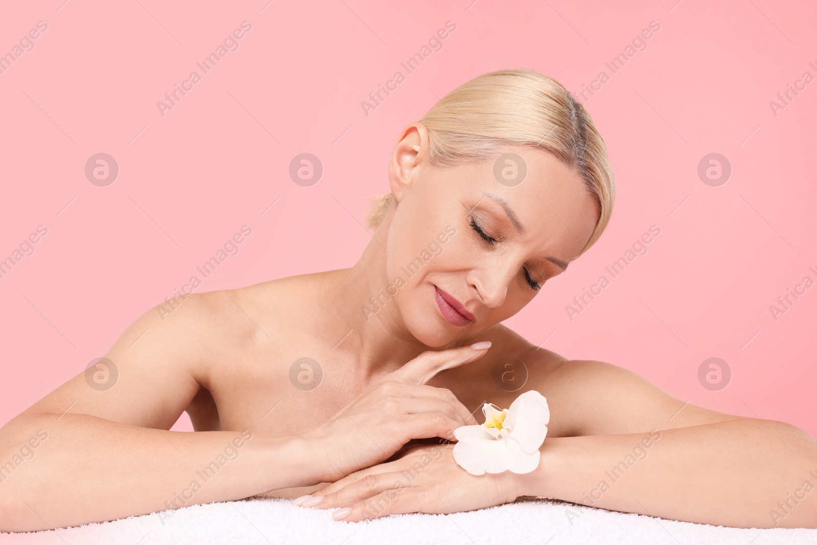 Beautiful woman with orchid flower and towel on light pink background Photo of Beautiful woman with orchid flower and towel on light pink background