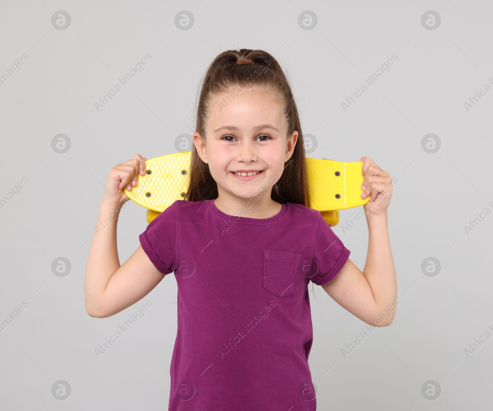 Little girl with penny board on light grey background Photo of Little girl with penny board on light grey background