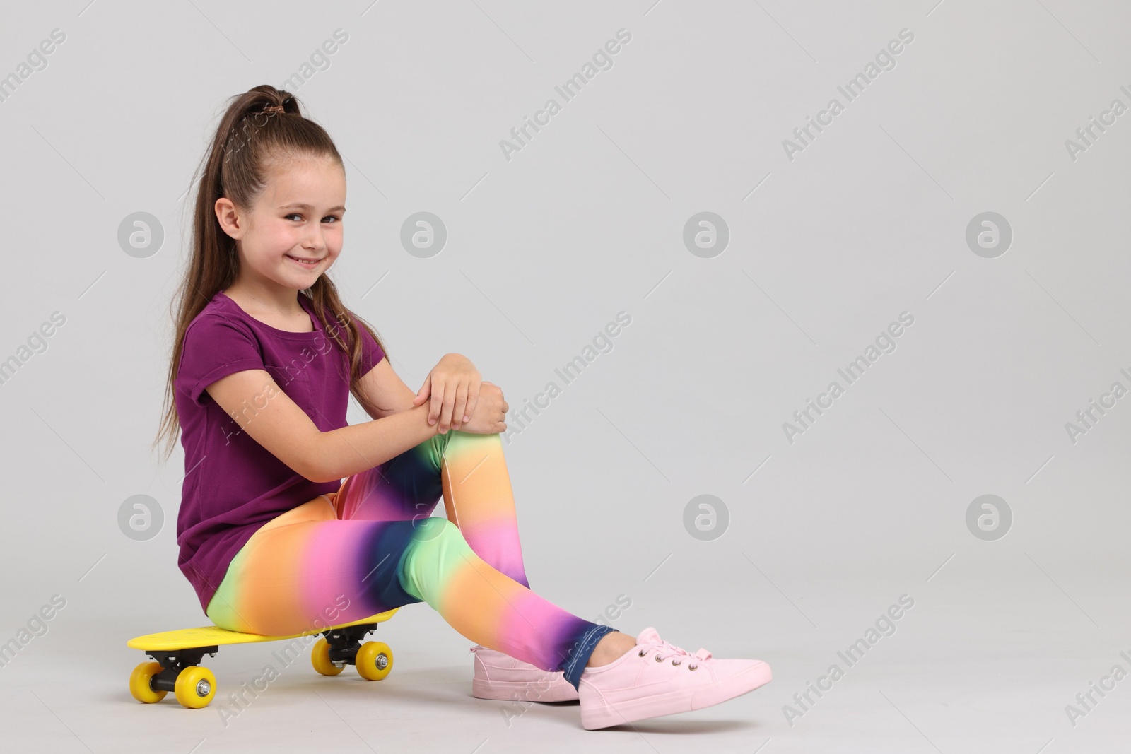 Little girl with penny board on light grey background, space for text Photo of Little girl with penny board on light grey background, space for text