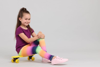 Photo of Little girl with penny board on light grey background, space for text