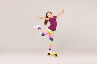 Photo of Little girl with penny board on light grey background