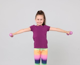 Photo of Little girl with dumbbells on light grey background