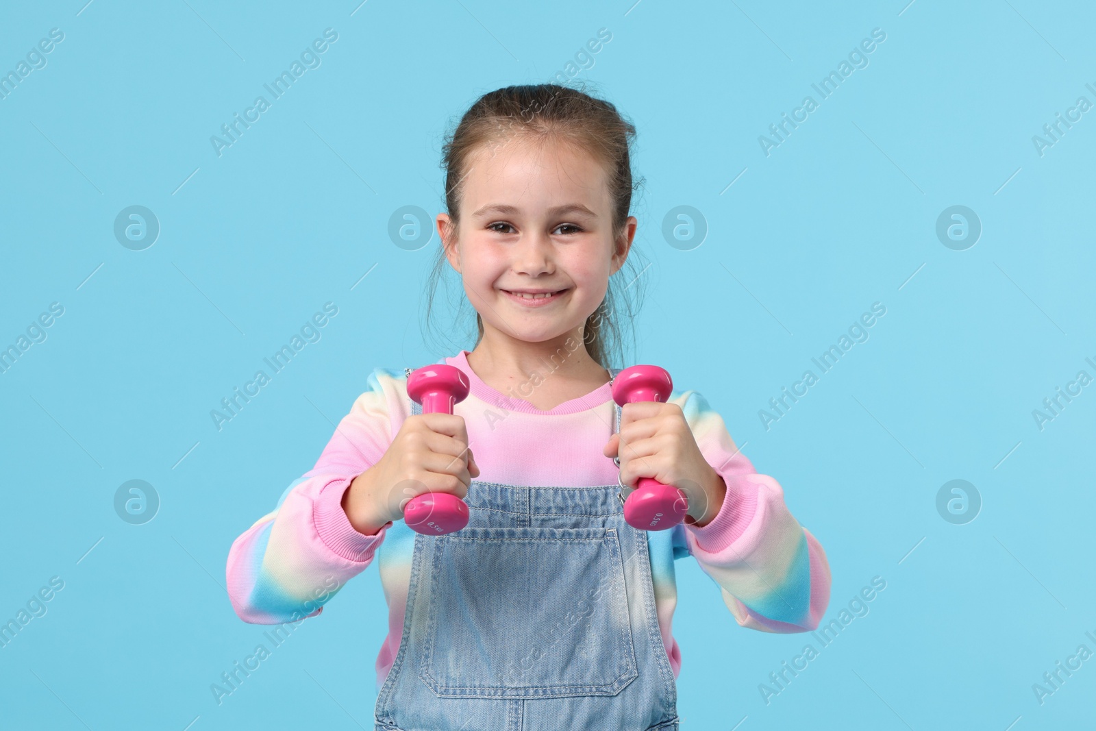 Little girl with dumbbells on light blue background Photo of Little girl with dumbbells on light blue background