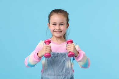 Photo of Little girl with dumbbells on light blue background