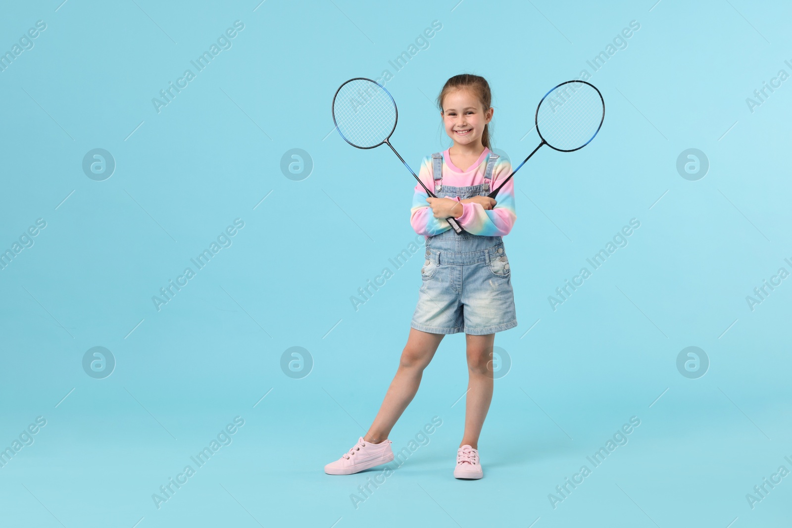 Little girl with tennis rackets on light blue background, space for text Photo of Little girl with tennis rackets on light blue background, space for text