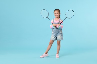Photo of Little girl with tennis rackets on light blue background, space for text