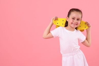 Photo of Little girl with penny board on pink background, space for text