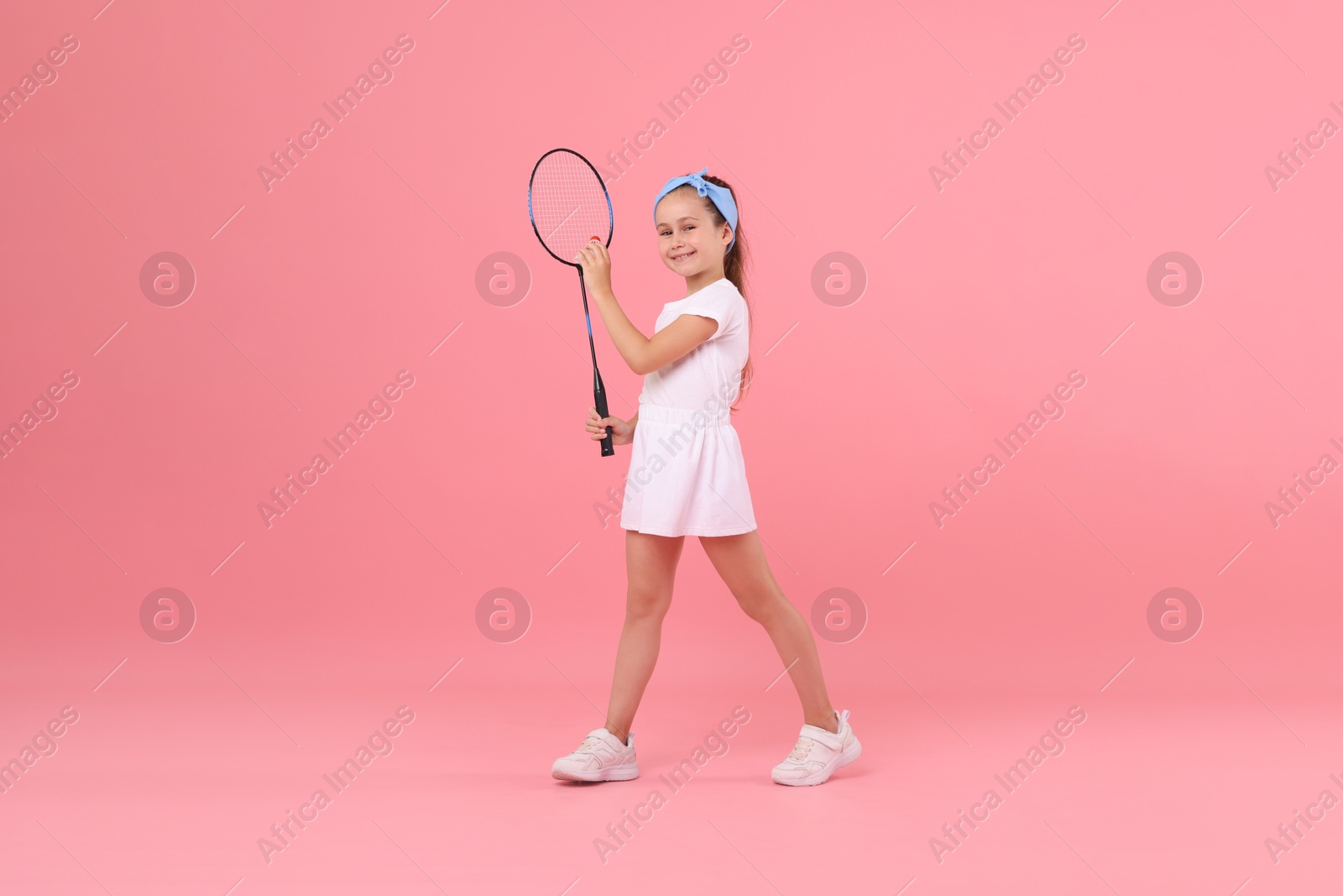 Little girl with tennis racket and shuttlecock on pink background Photo of Little girl with tennis racket and shuttlecock on pink background