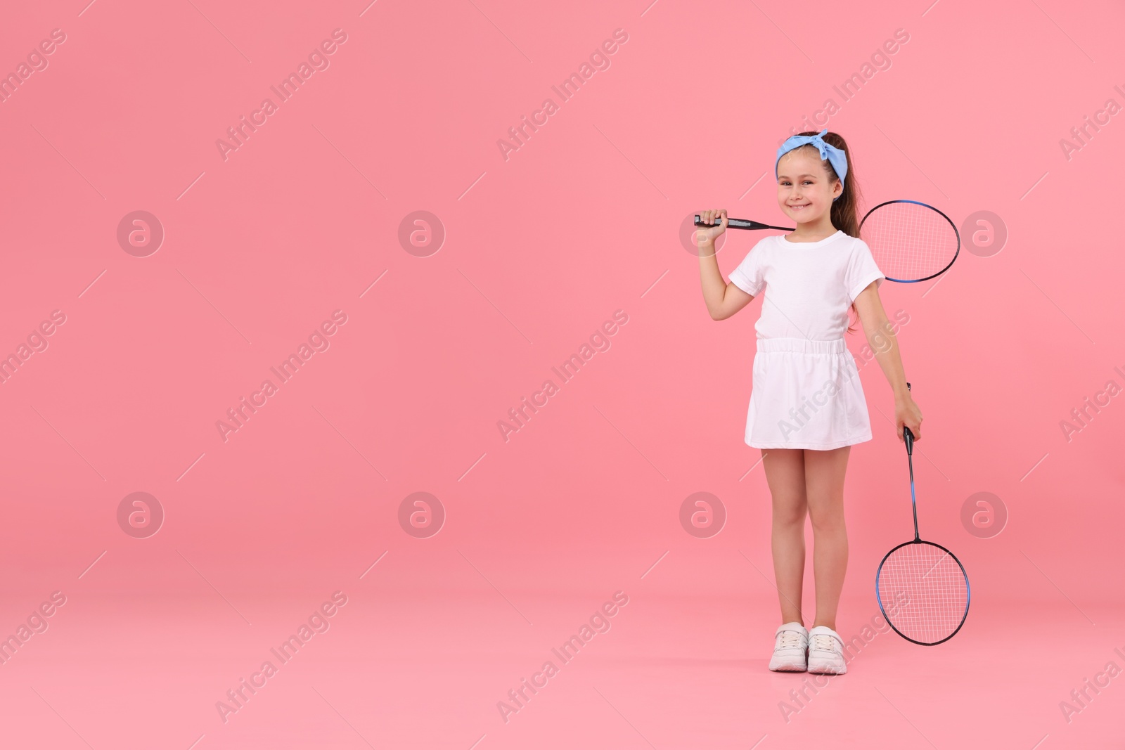 Little girl with tennis rackets on pink background, space for text Photo of Little girl with tennis rackets on pink background, space for text