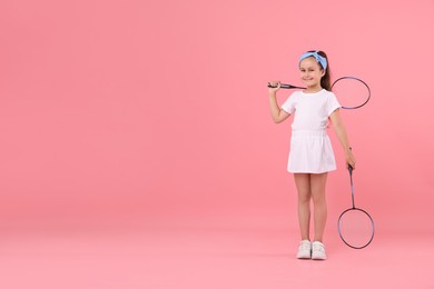 Photo of Little girl with tennis rackets on pink background, space for text