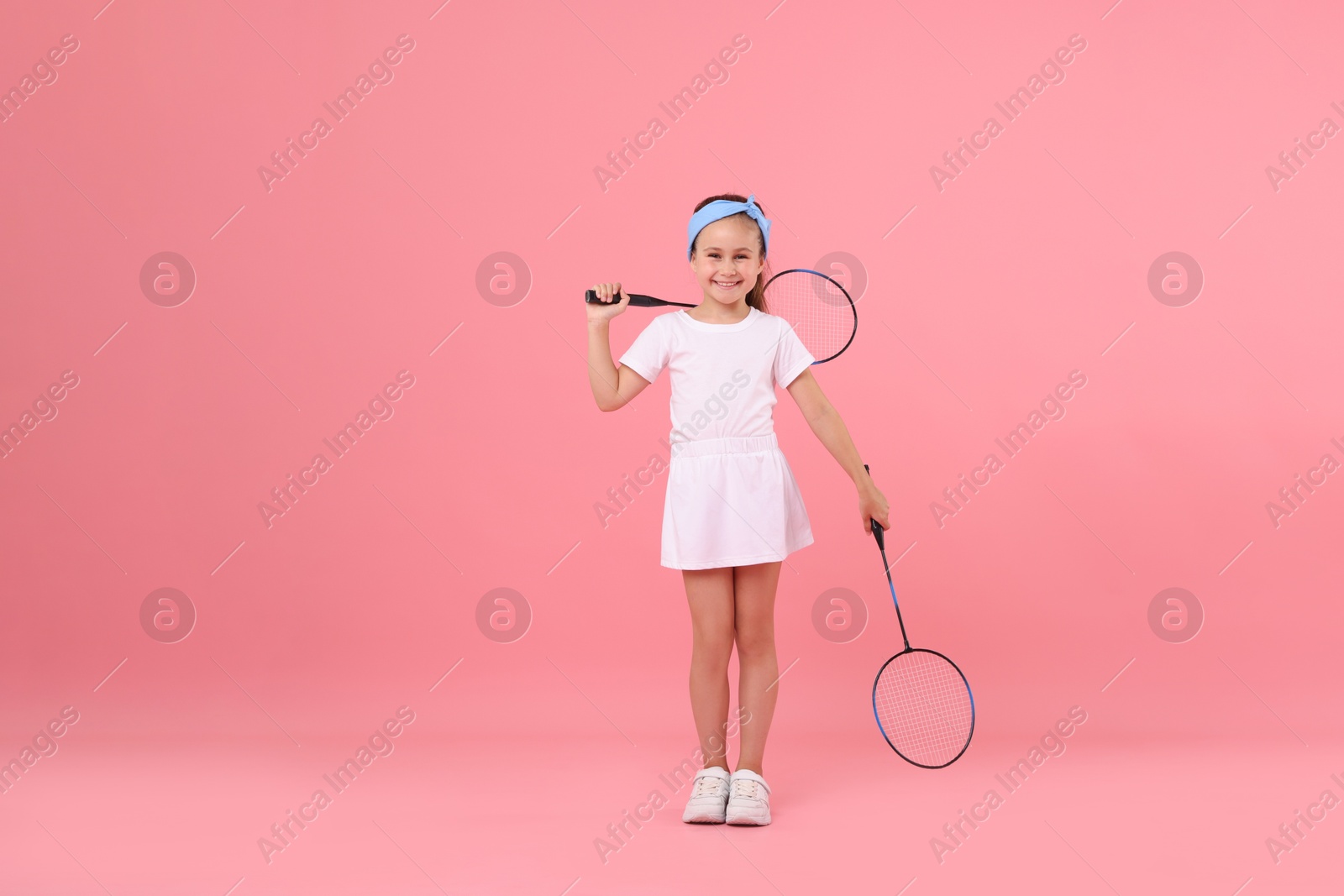 Little girl with tennis rackets on pink background Photo of Little girl with tennis rackets on pink background