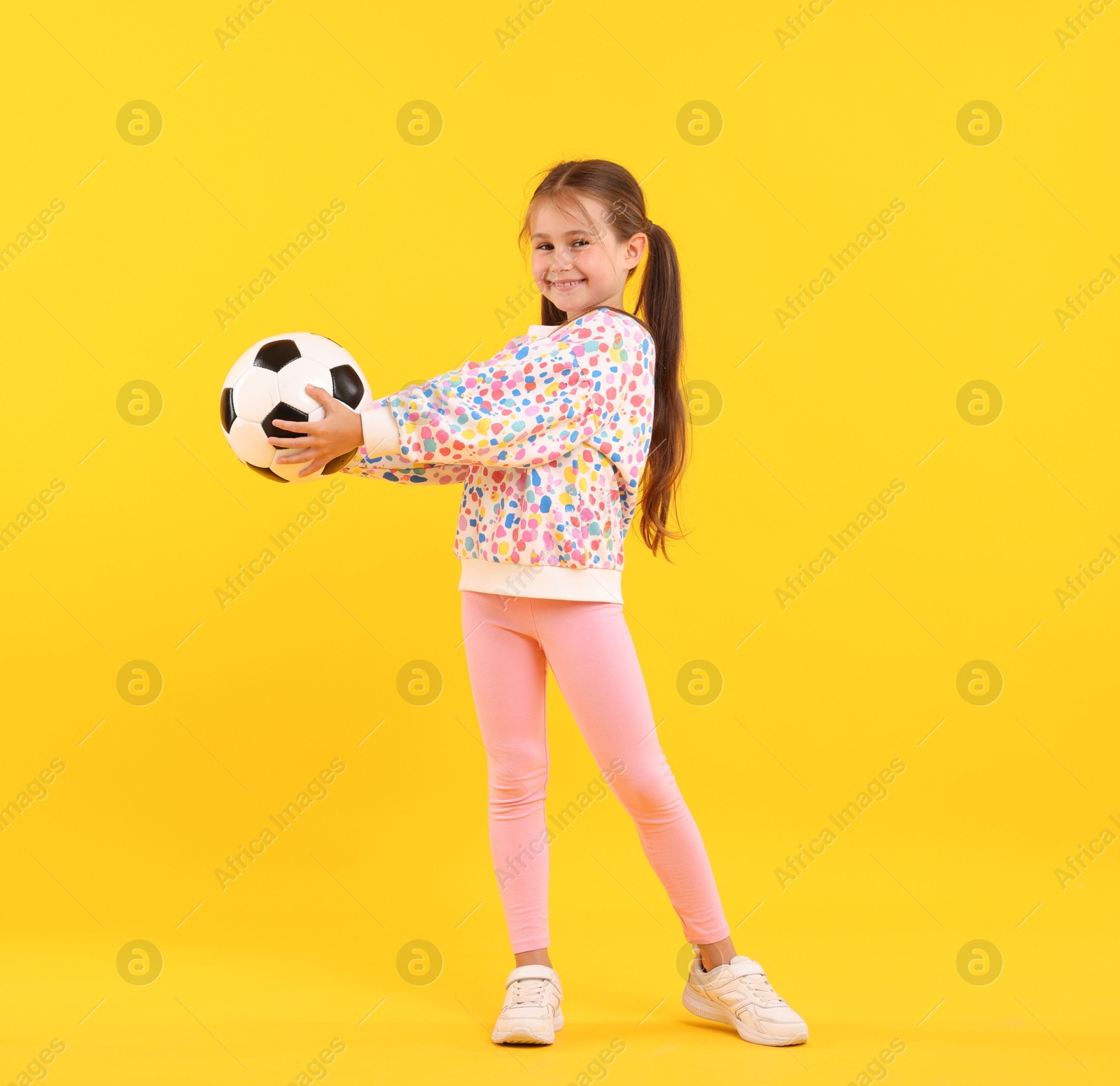 Little girl with soccer ball on yellow background Photo of Little girl with soccer ball on yellow background