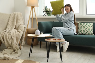 Image of Emotional young woman with pillow looking in disgust at cockroaches on table at home