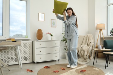 Image of Emotional young woman with pillow frightened by cockroaches on floor at home