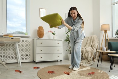 Image of Emotional young woman with pillow frightened by cockroaches on floor at home