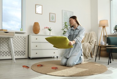 Image of Emotional young woman with pillow frightened by cockroaches on floor at home