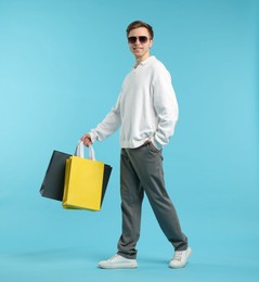 Photo of Cheerful man with shopping bags on light blue background