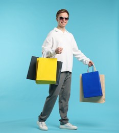 Photo of Cheerful man with shopping bags on light blue background