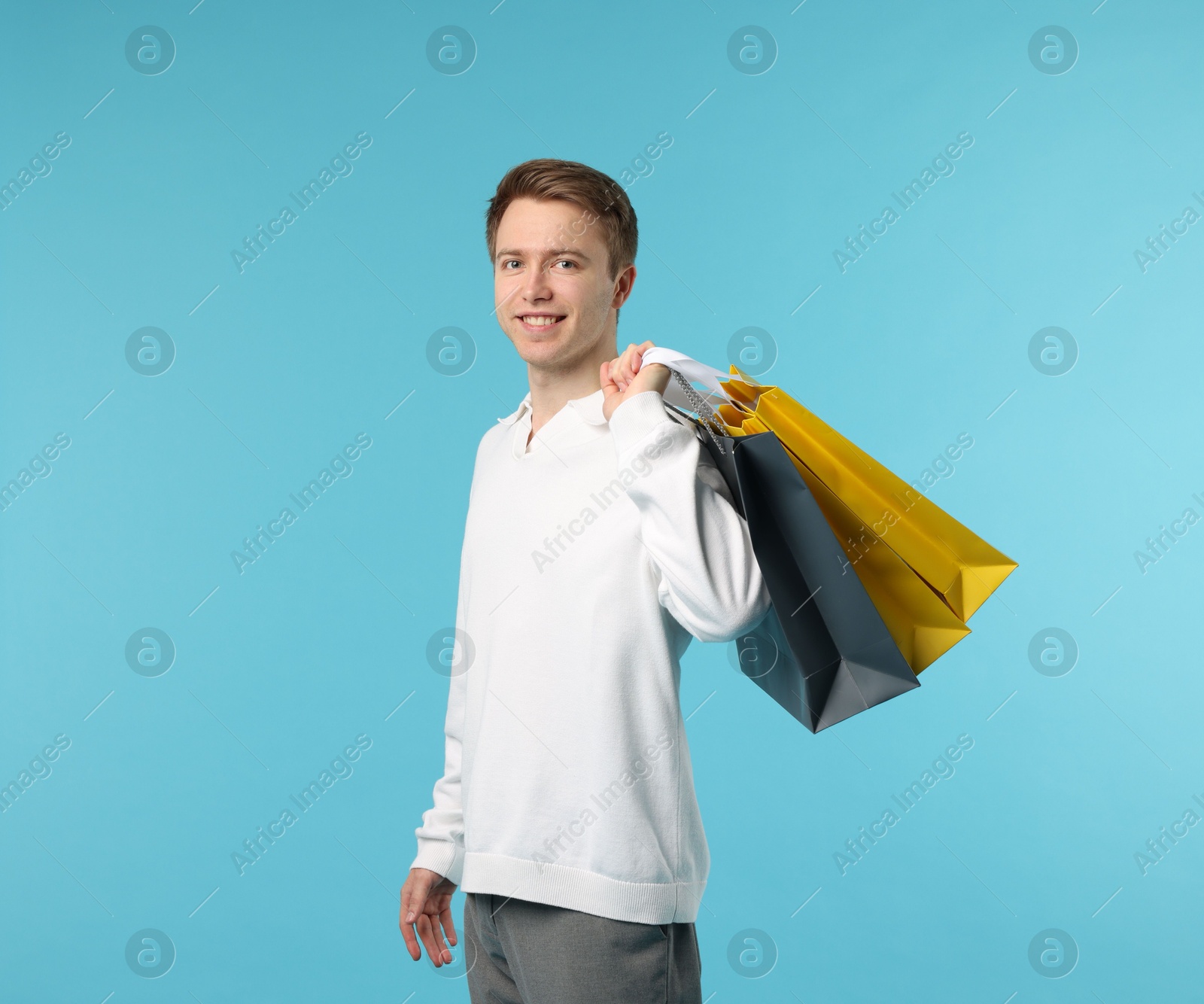 Cheerful man with shopping bags on light blue background Photo of Cheerful man with shopping bags on light blue background