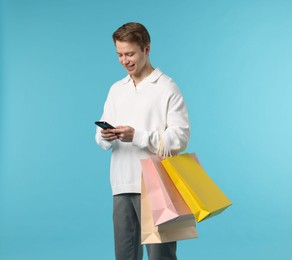 Photo of Cheerful man with smartphone and shopping bags on light blue background