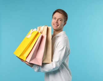 Photo of Cheerful man with shopping bags on light blue background