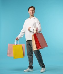 Photo of Cheerful man with shopping bags on light blue background