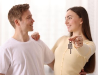 Photo of Happy couple with key of their new house indoors, selective focus