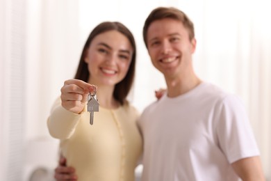 Photo of Happy couple with key of their new house indoors, selective focus