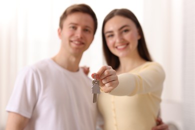 Photo of Happy couple with key of their new house indoors, selective focus
