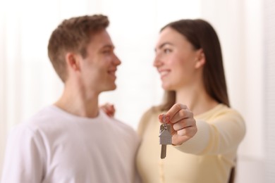 Photo of Happy couple with key of their new house indoors, selective focus