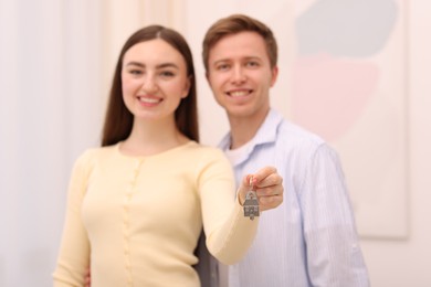 Photo of Happy couple with key of their new house indoors, selective focus