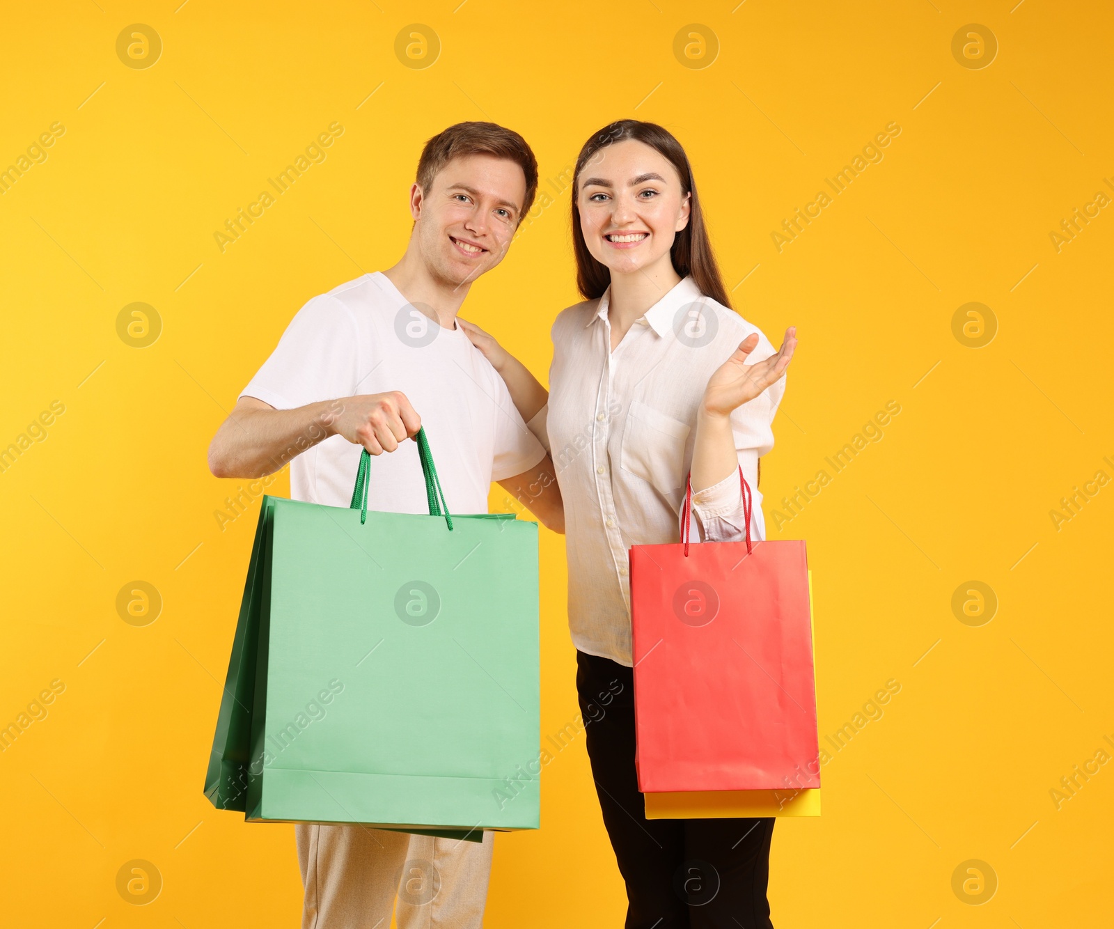 Happy couple with shopping bags on yellow background Photo of Happy couple with shopping bags on yellow background