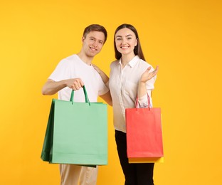 Photo of Happy couple with shopping bags on yellow background