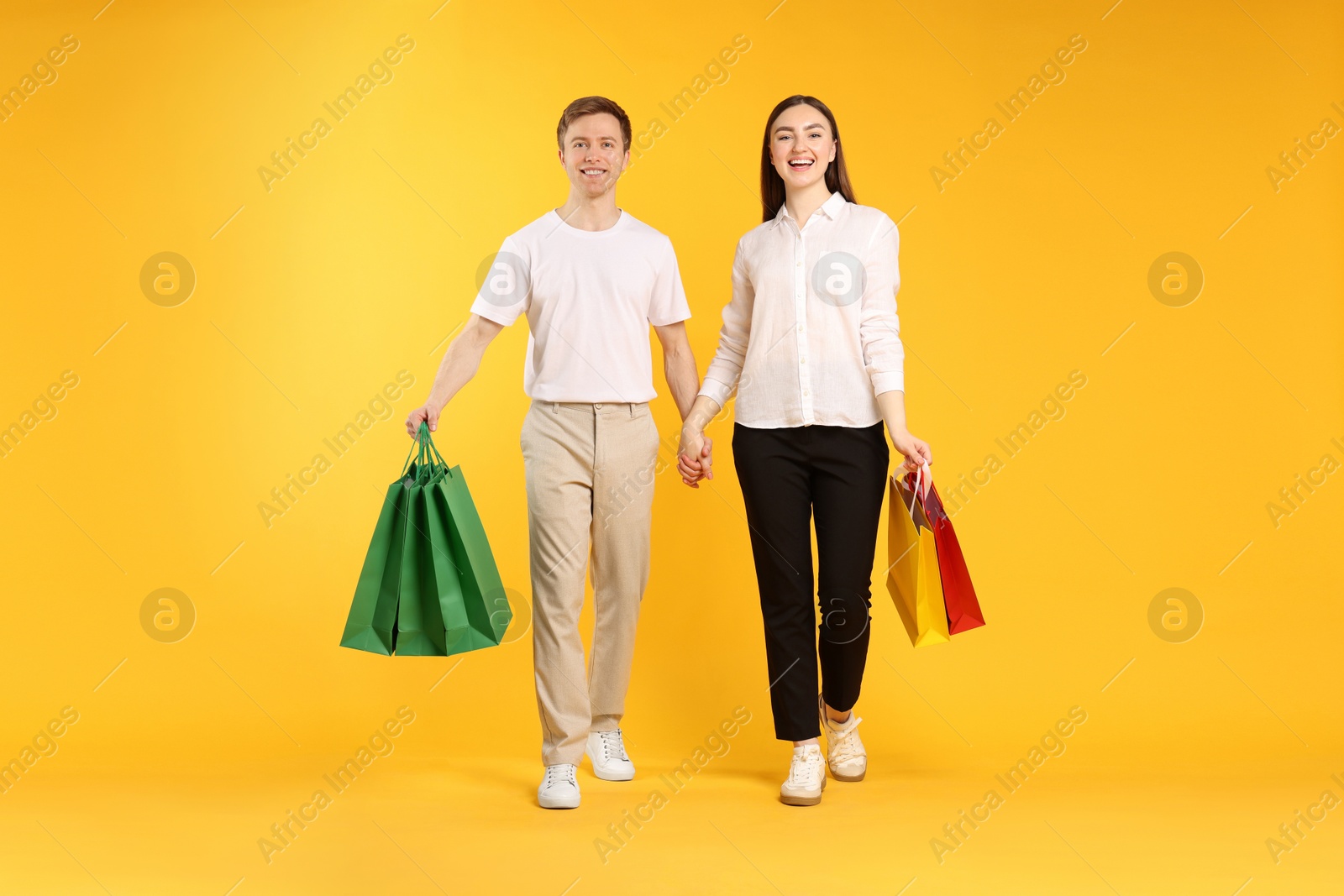 Happy couple with shopping bags on yellow background Photo of Happy couple with shopping bags on yellow background