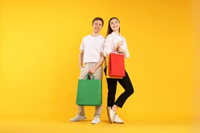 Photo of Happy couple with shopping bags on yellow background