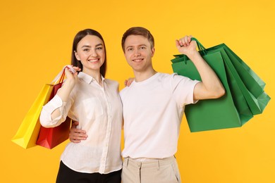 Photo of Happy couple with shopping bags on yellow background