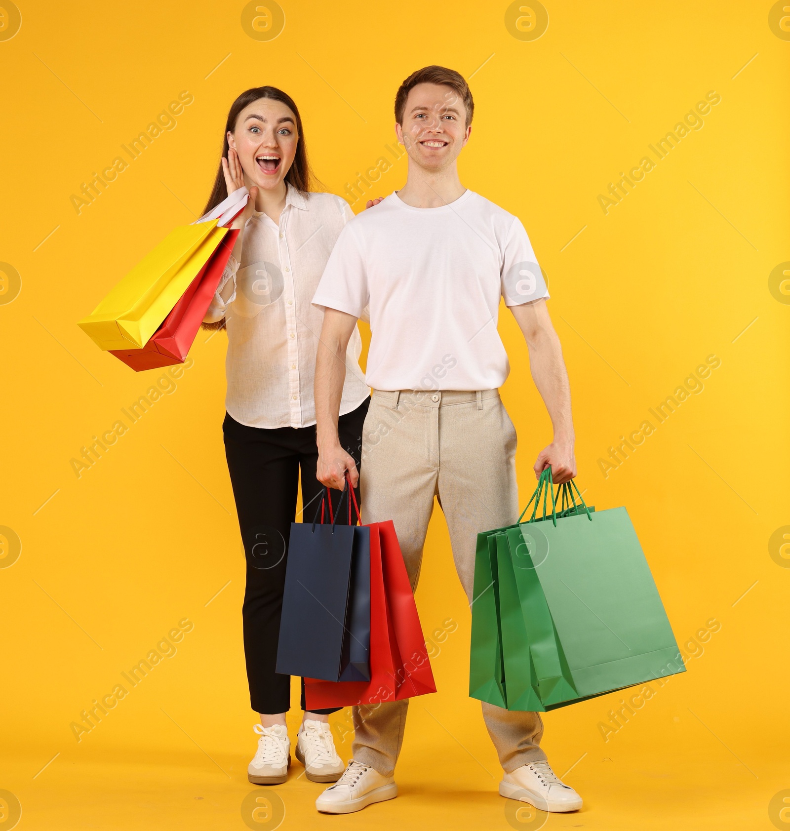 Happy couple with shopping bags on yellow background Photo of Happy couple with shopping bags on yellow background
