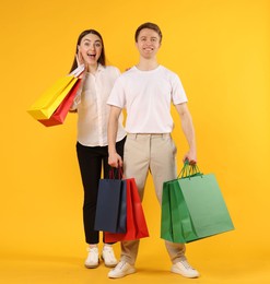 Photo of Happy couple with shopping bags on yellow background