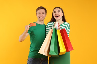 Photo of Happy couple with credit card and shopping bags on yellow background