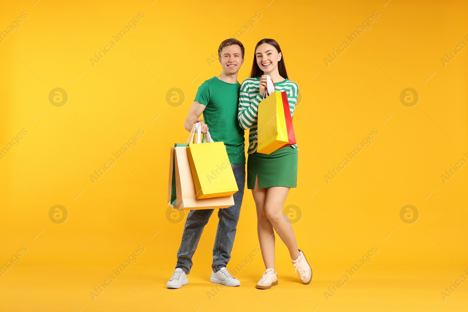 Photo of Happy couple with shopping bags on yellow background
