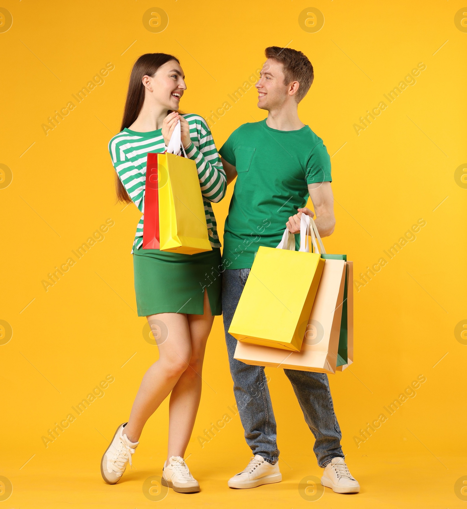 Happy couple with shopping bags on yellow background Photo of Happy couple with shopping bags on yellow background