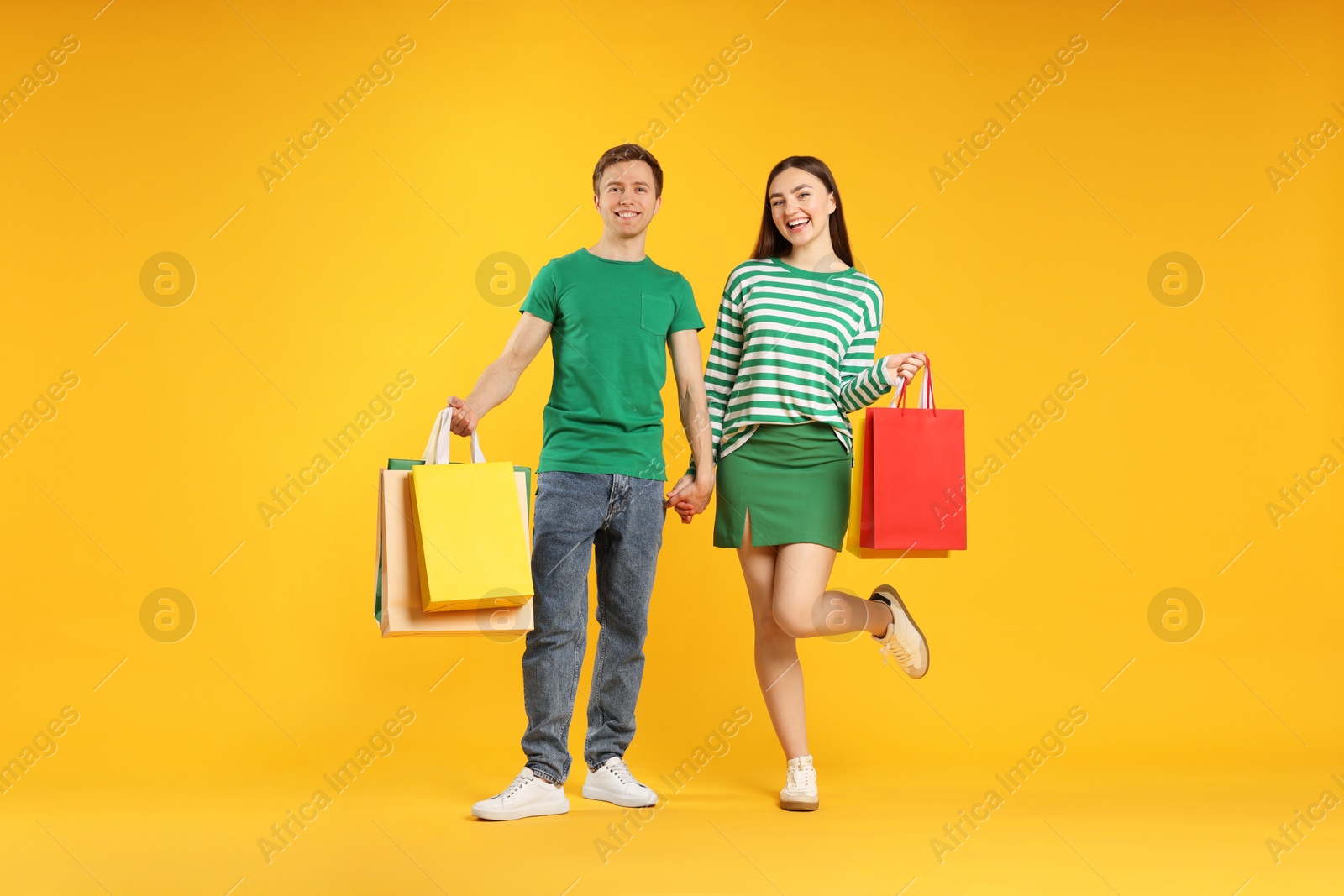 Happy couple with shopping bags on yellow background Photo of Happy couple with shopping bags on yellow background