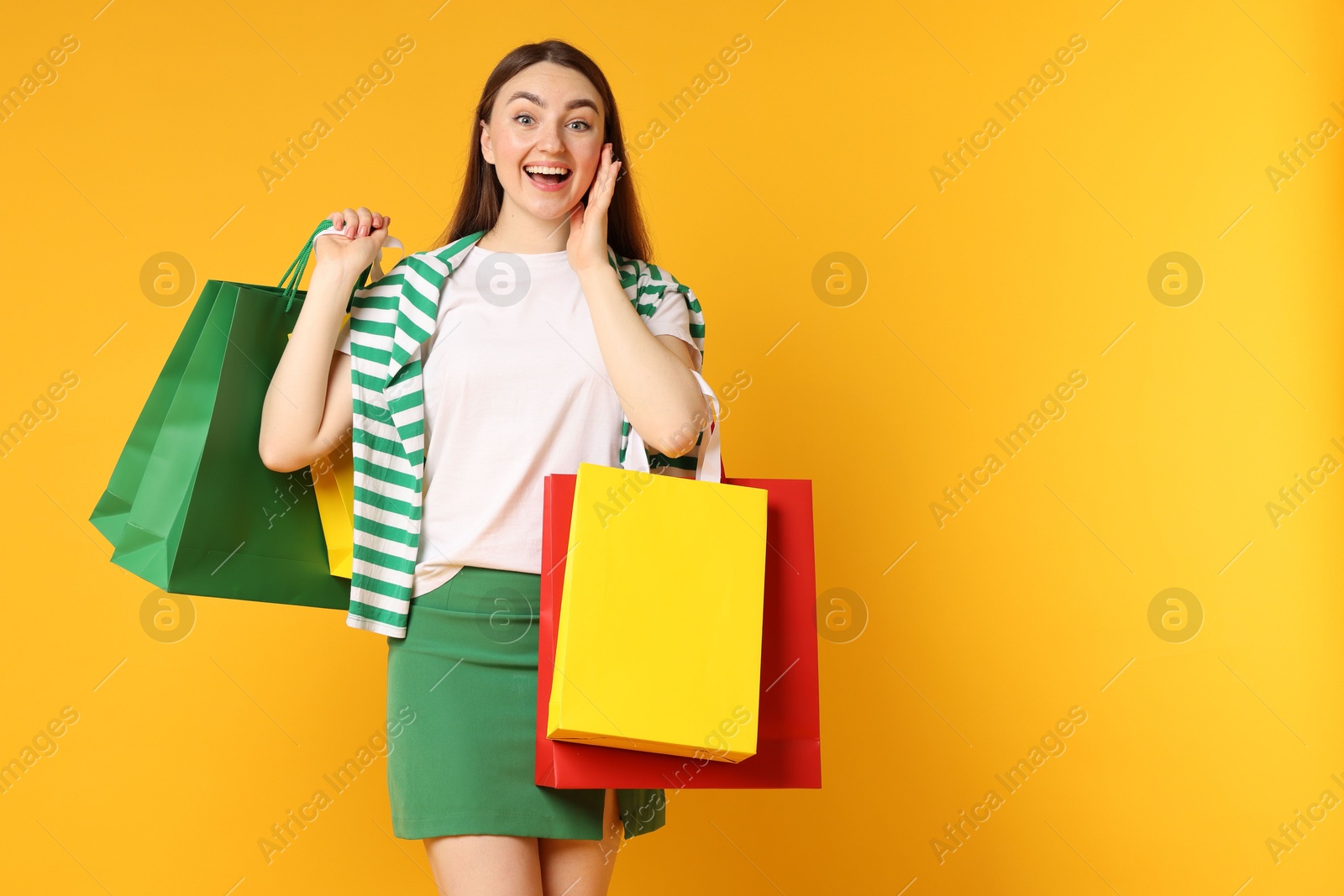 Excited woman with shopping bags on yellow background Photo of Excited woman with shopping bags on yellow background