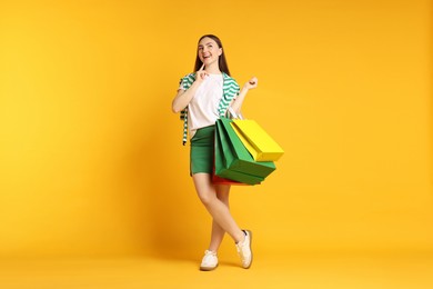 Photo of Positive woman with shopping bags on yellow background