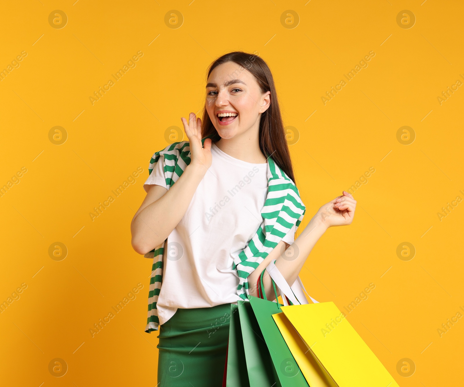 Excited woman with shopping bags on yellow background Photo of Excited woman with shopping bags on yellow background